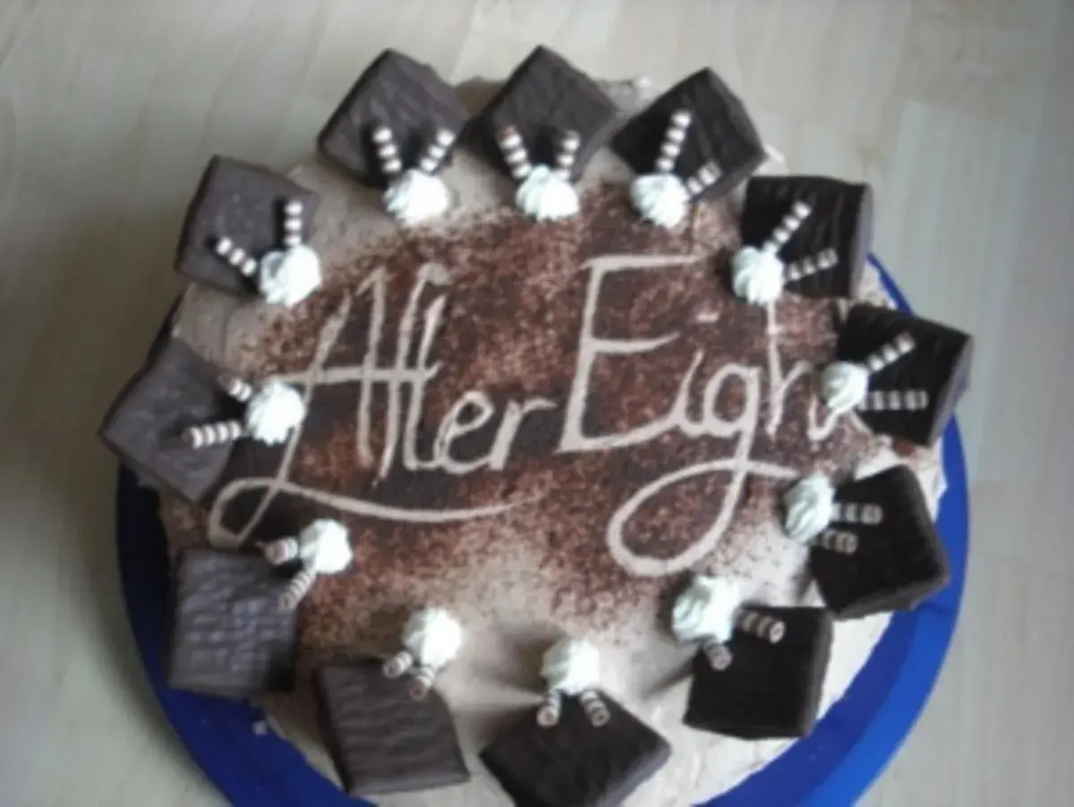 Eine After Eight Torte mit Schokoladenquadraten und Sahnetuffs. Der Schriftzug "After Eight" ist in Kakao auf die Torte gestreut.