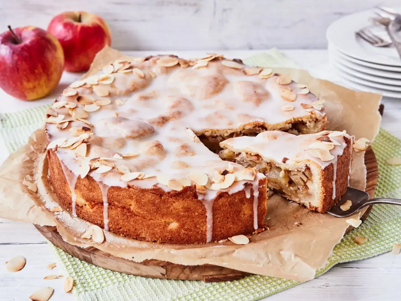 Ein köstlicher gedeckter Apfelkuchen mit zarter Glasur und Mandelblättchen, daneben ein Stück Apfelmus.