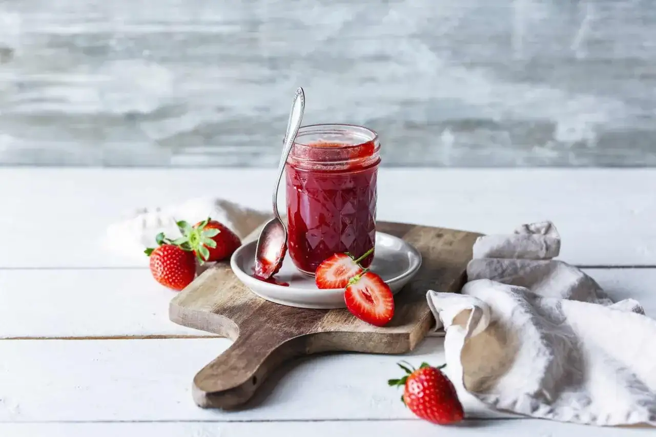Frische Erdbeeren und selbstgemachte Erdbeermarmelade aus dem Thermomix auf einem Holzbrett.
