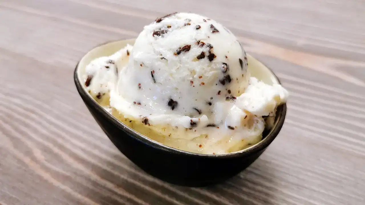 Ein Löffel cremiges Stracciatella Eis mit zarten Schokoladenstückchen in einer Schale auf Holzhintergrund.