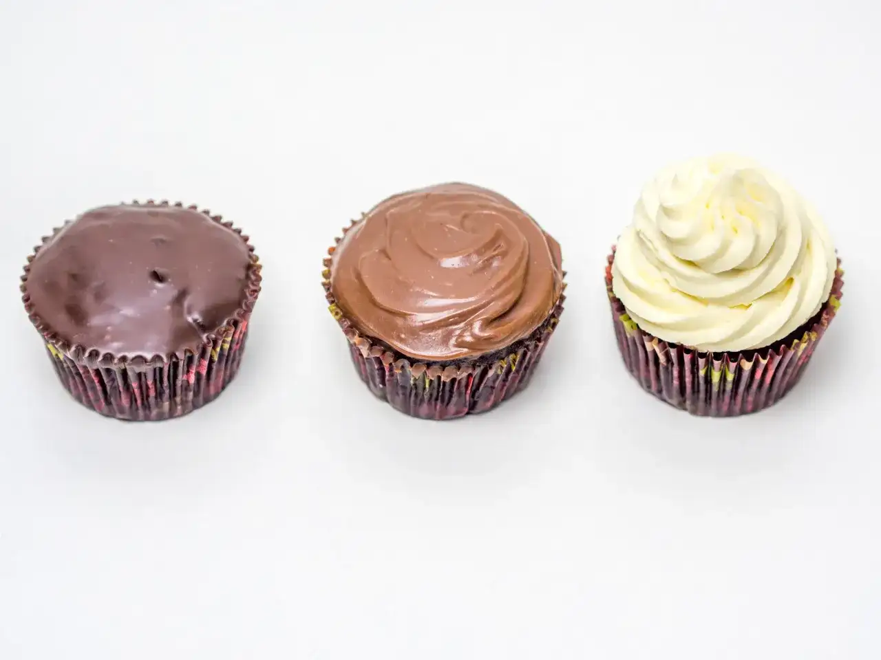 Drei Cupcakes: einer mit dunkler Ganache, einer mit Milchschokoladen-Ganache und einer mit weißer Creme. Perfekt für ein schnelles Ganache Rezept.