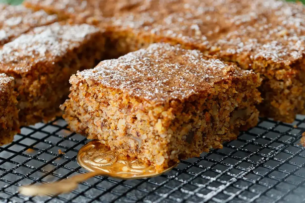 Ein saftiger karottenkuchen glutenfrei, bestäubt mit Puderzucker, wird auf einem Gitter präsentiert.