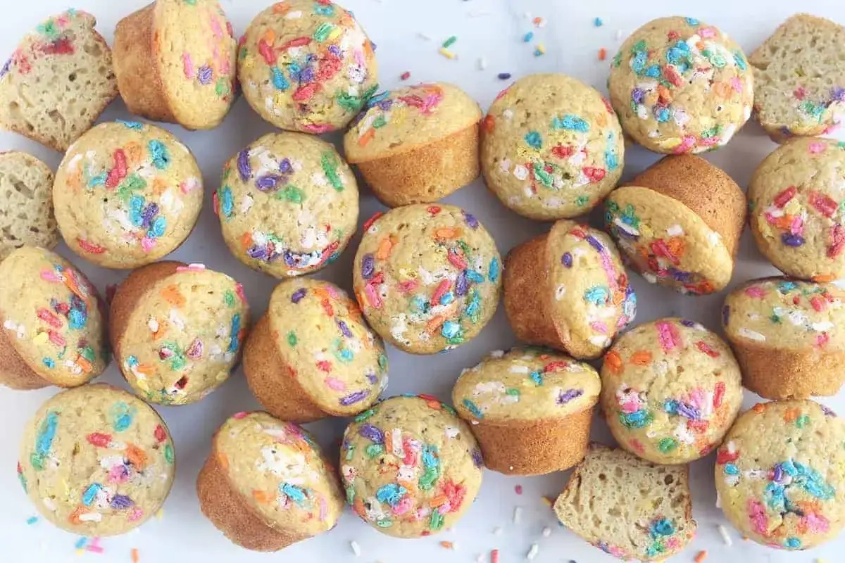 Bunte Muffins mit Streuseln, perfekt für einen Kindergeburtstag. Einige sind angeschnitten und zeigen den lockeren Teig.
