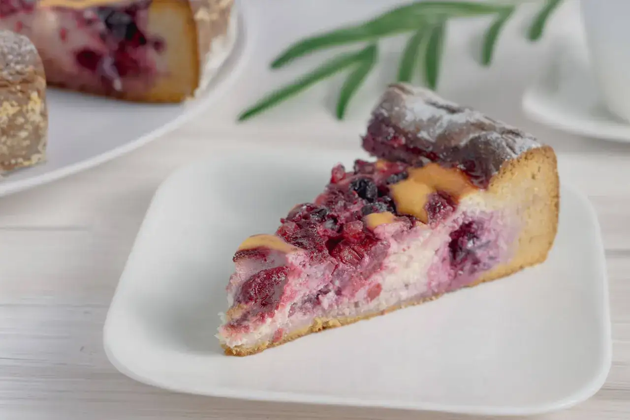 Ein Stück saftiger low carb kuchen mit Beeren und Puderzucker auf einem weißen Teller.