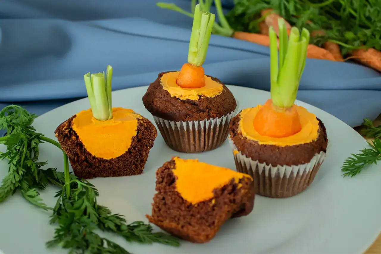 Schokoladen-Oster-Muffins mit orangefarbener Glasur und einem kleinen Karottenstück mit Grün als Dekoration.