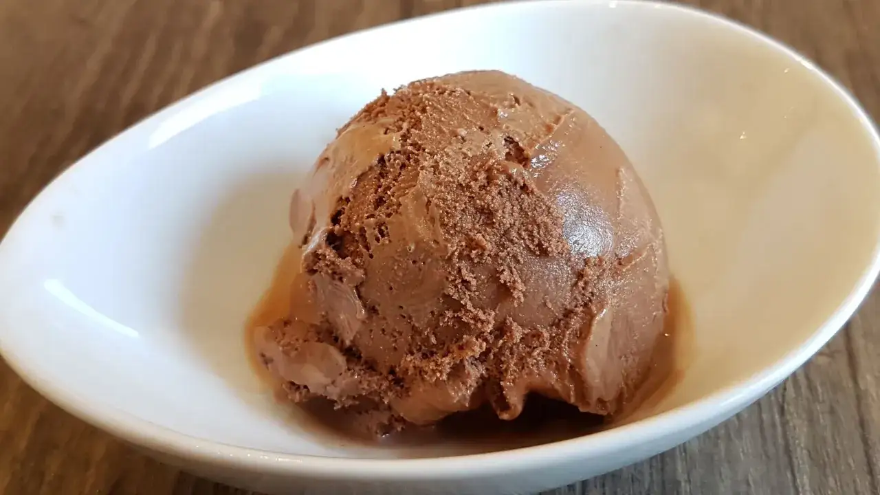 Ein Löffel cremiges Schokoladen-Eis schmilzt in einer weißen Schale.