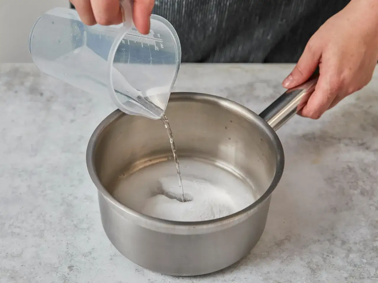 Wasser wird zu Zucker in einem Topf gegossen. So einfach kann man Glukosesirup selber machen.
