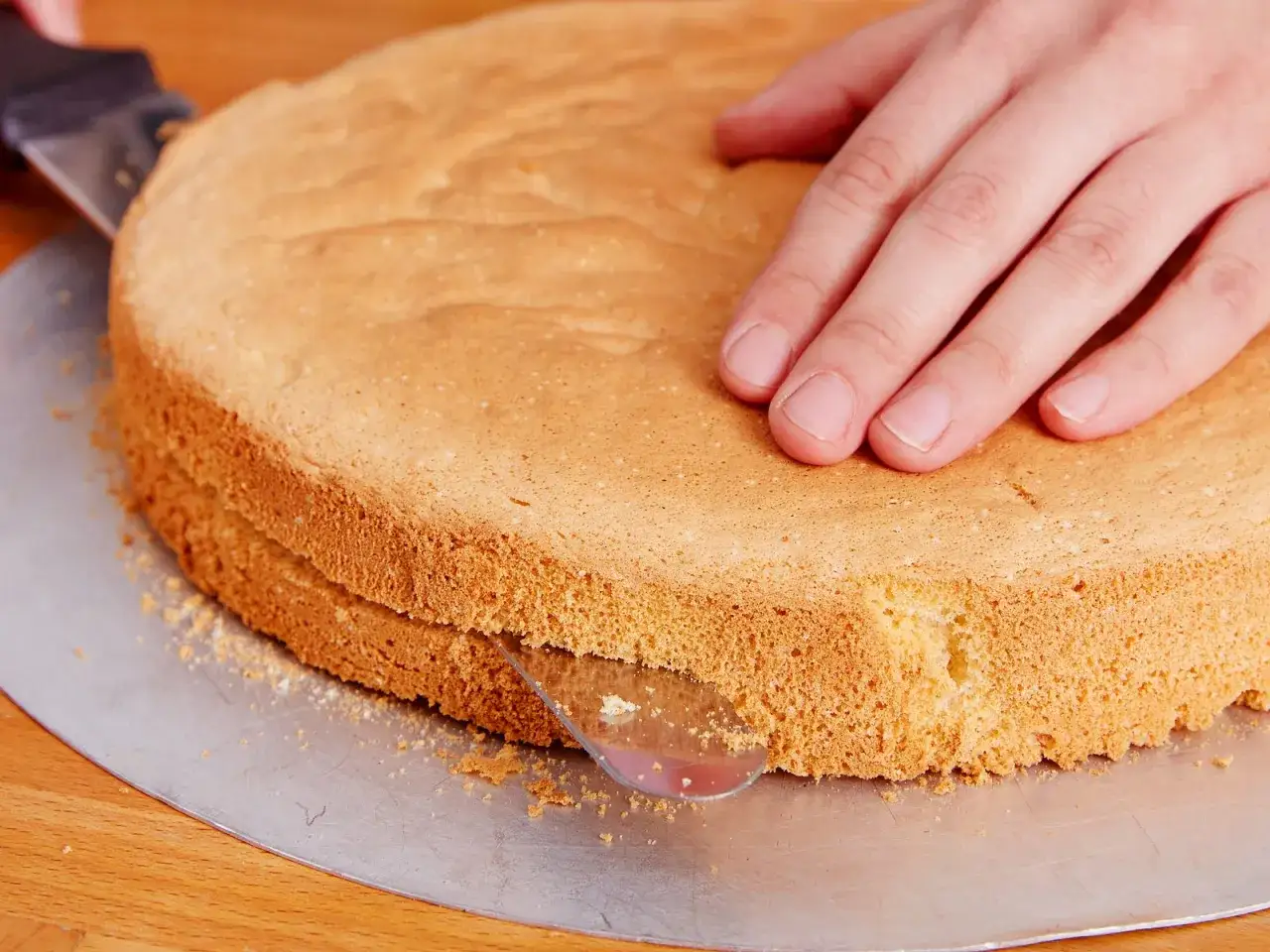 Ein Biskuitteig-Rezept für die Springform wird hier perfekt umgesetzt. Eine Hand hält den Kuchen, während ein Messer ihn teilt.