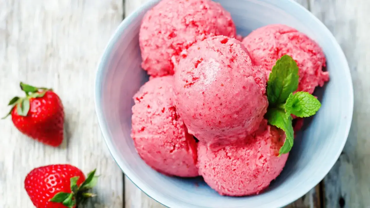 Sch&uuml;ssel mit erfrischendem Erdbeereis mit Sahne, garniert mit Minze. Daneben liegen frische Erdbeeren.