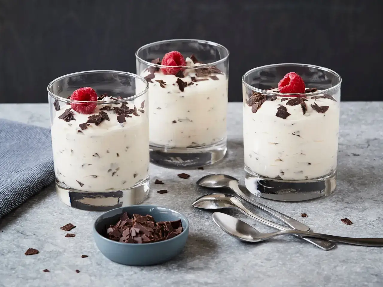 Drei Gl&auml;ser mit cremiger Herrencreme, garniert mit Himbeeren und Schokost&uuml;ckchen. Ein kleines Sch&auml;lchen mit Schokost&uuml;ckchen und L&ouml;ffel daneben.