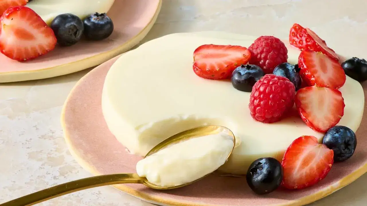 Cremige Panna Cotta, garniert mit frischen Erdbeeren, Himbeeren und Blaubeeren, auf einem Löffel.