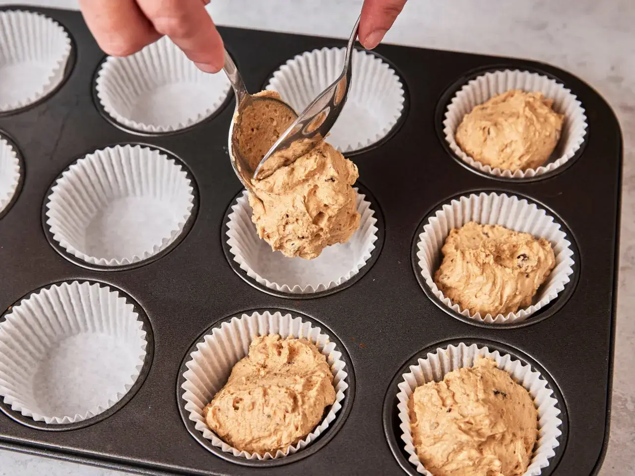 Hände portionieren Teig mit Löffeln in Muffinförmchen. Das Backen von Muffins beginnt!