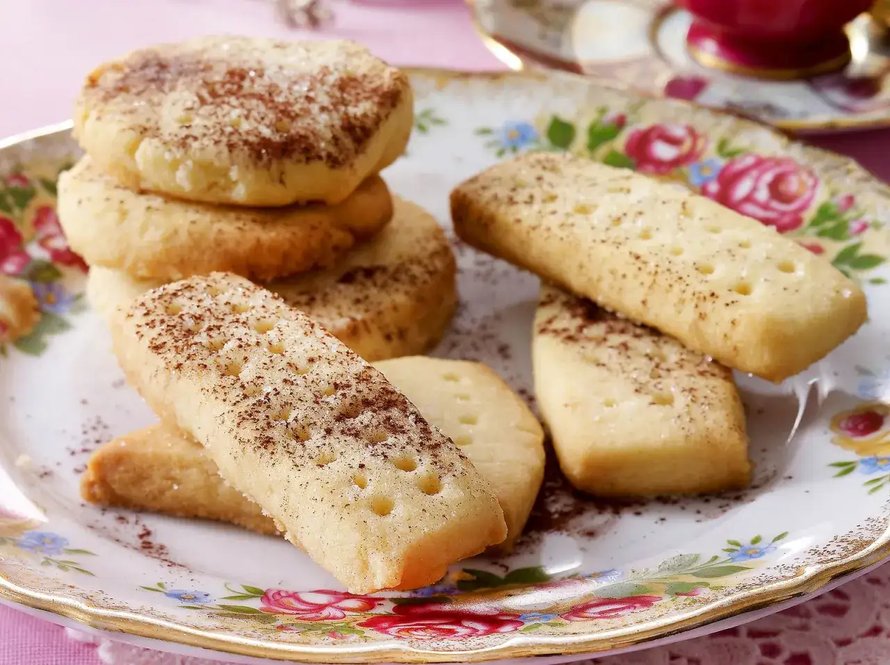 Leckeres Shortbread-Rezept: Runde und rechteckige Kekse, bestreut mit Zucker und Zimt, auf einem floralen Teller.