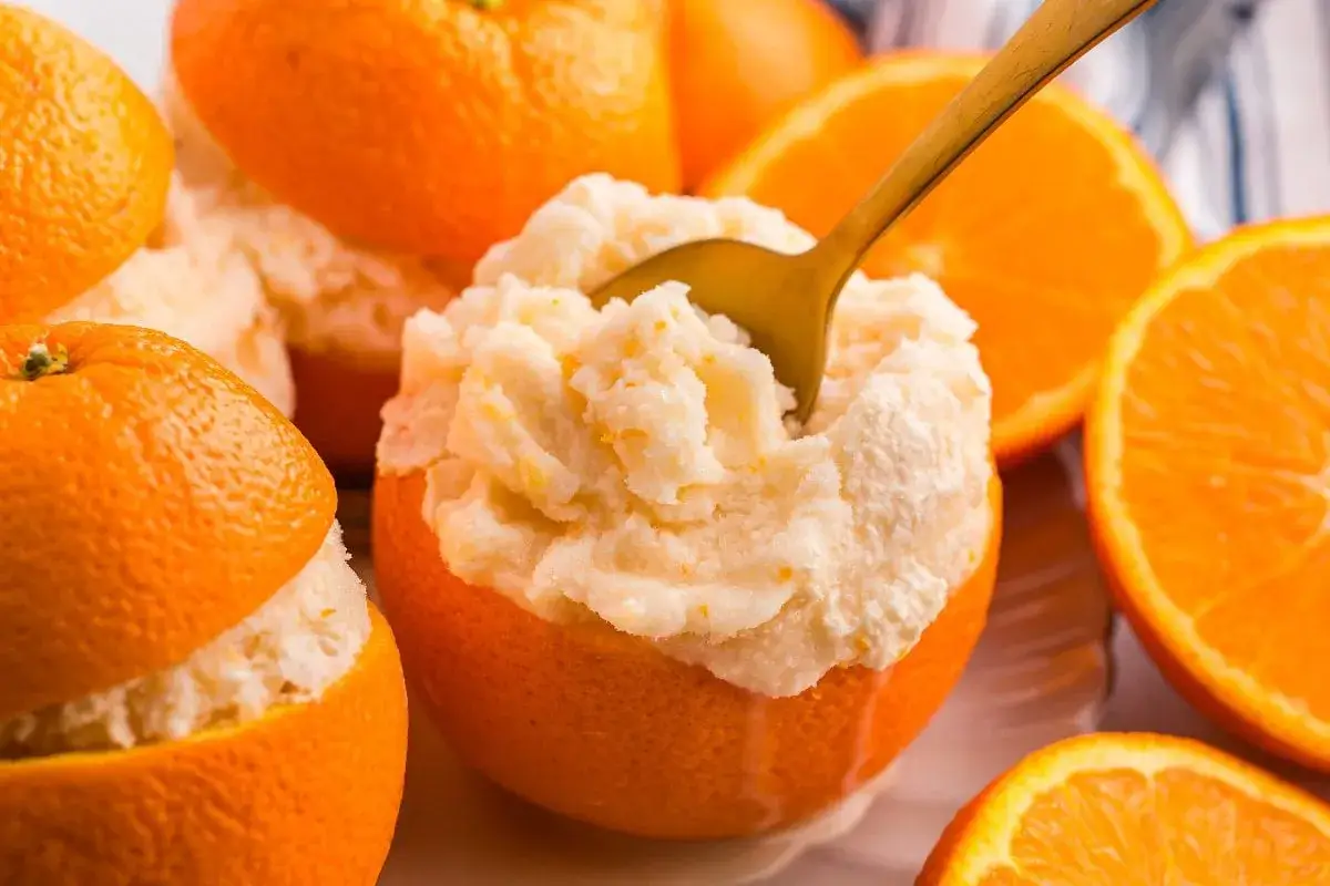 Erfrischendes orangen sorbet, serviert in ausgehöhlten Orangen. Eine goldene Löffelspitze ragt aus dem cremigen Dessert.