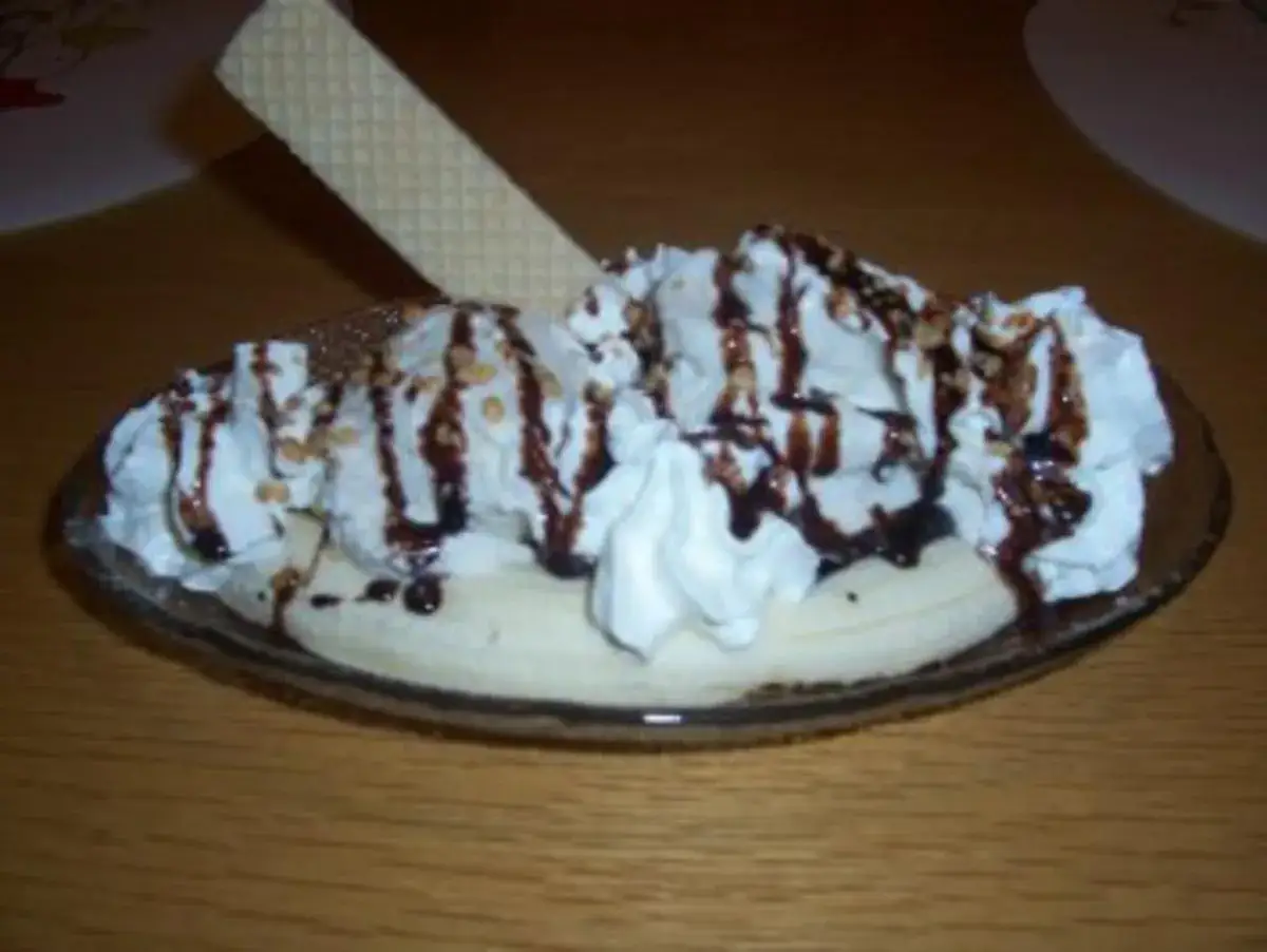 Ein köstlicher Bananensplit Eis mit Sahne, Schokoladensauce und Nüssen, garniert mit einer Waffel.