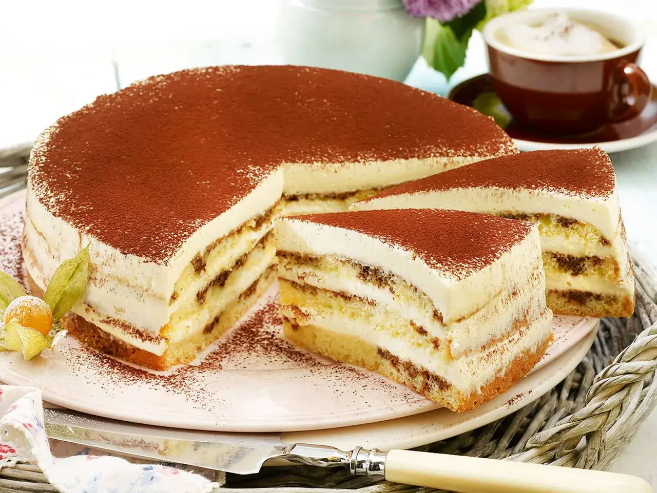 Eine köstliche Cappuccino Torte, mit Kakao bestäubt, auf einem Teller mit einem Stück abgetrennt. Daneben eine Tasse Kaffee.