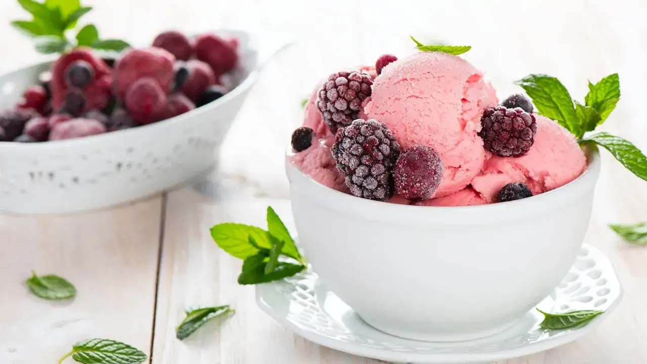 Schüssel mit rosa Buttermilch-Frisch-Eis, garniert mit gefrorenen Beeren und Minze.