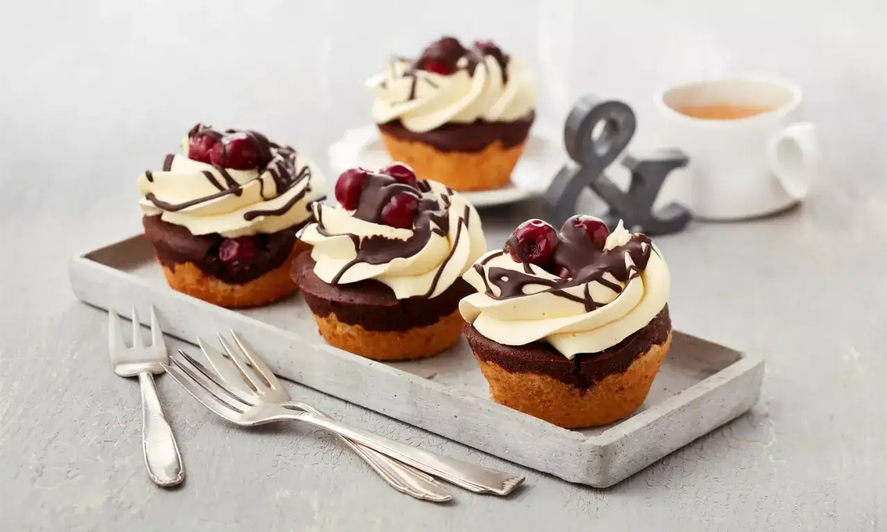 Vier köstliche Donauwellen Muffins mit Sahne, Kirschen und Schokoglasur auf einem Tablett.
