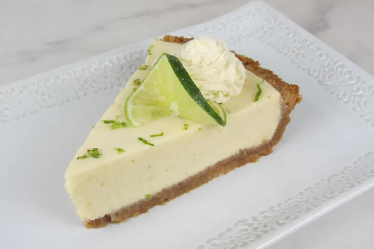 Ein Stück cremiger Key Lime Pie mit Limettenscheibe und Sahnetupfer auf einem verzierten Teller.
