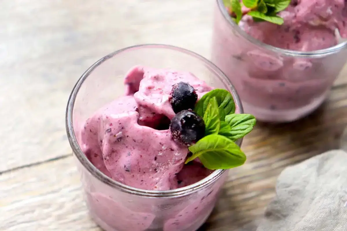 Cremiges Bananen-Eis mit Beeren und Minze in Gläsern serviert. Ein erfrischender Genuss!