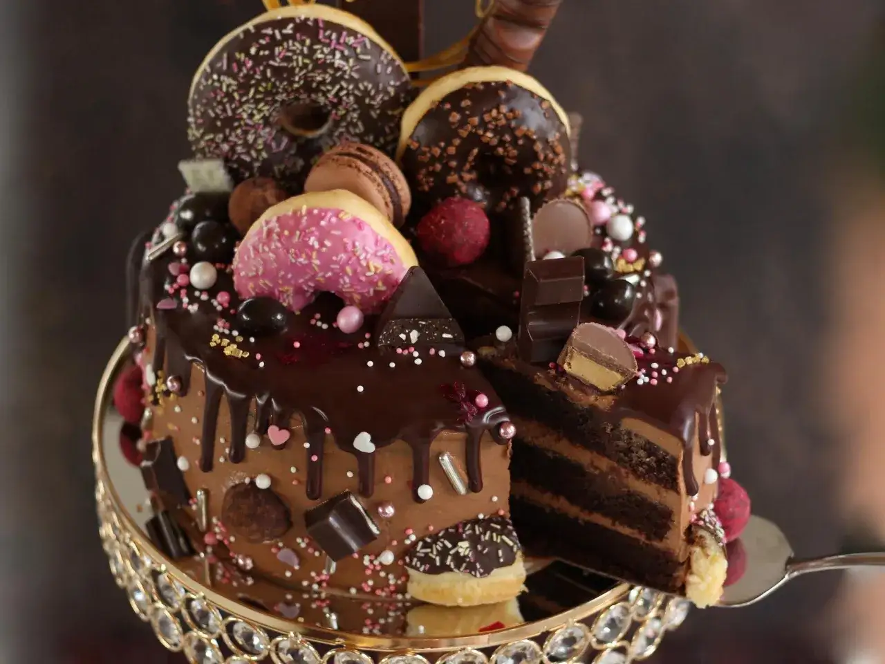 Eine &uuml;ppige Nutella Torte, dekoriert mit Donuts, Macarons und Schokoladenst&uuml;ckchen, pr&auml;sentiert sich auf einem goldenen Tortenst&auml;nder.