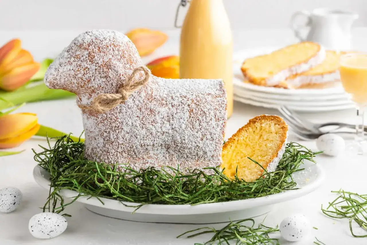 Ein süßer Osterlamm-Kuchen, bestäubt mit Puderzucker, liegt auf grünem Gras. Ein perfektes Osterlamm Rezept für das Fest.