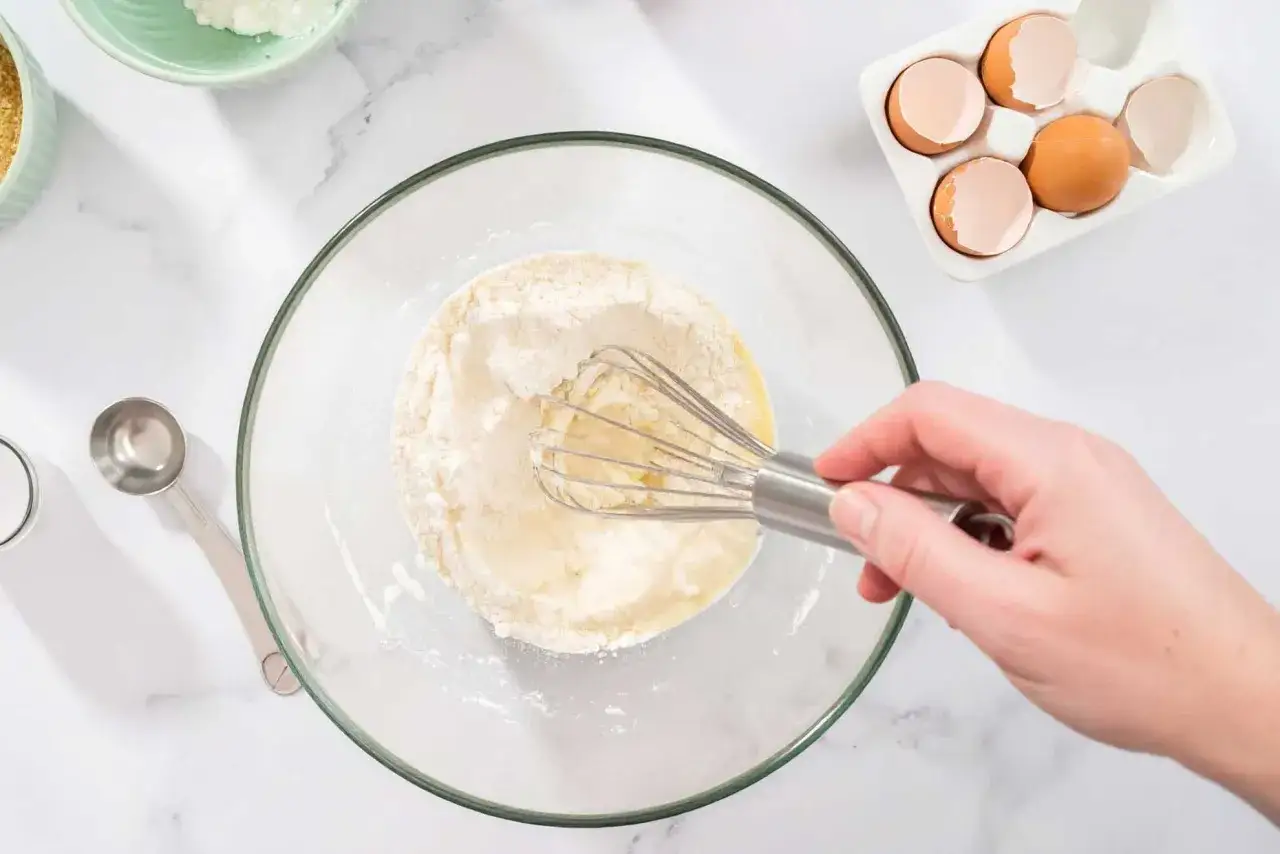 Hand mixt Mehl und Eier für leckere Torten Rezepte. Zutaten wie Zucker und Eierschalen liegen bereit.