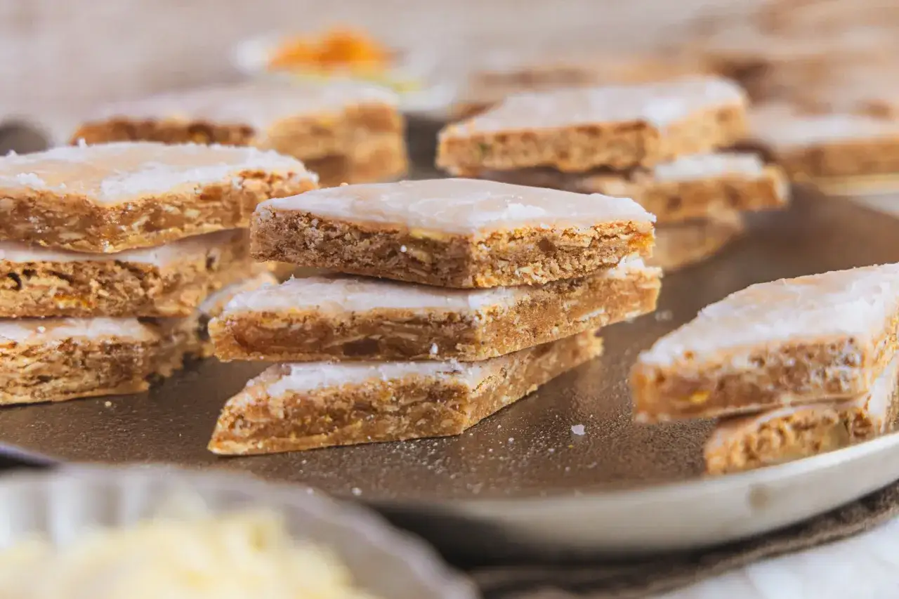 Stapel von Basler Leckerli, die nach einem traditionellen basler leckerli rezept gebacken wurden, mit Zuckerguss &uuml;berzogen und auf einem Teller angerichtet.