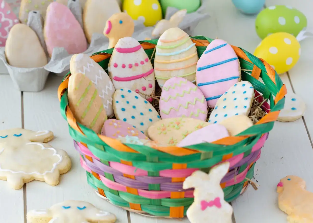 Bunte Osterkekse zum Ausstechen, liebevoll verziert, liegen in einem geflochtenen Korb. Hasen und Küken-Kekse zieren den Tisch.