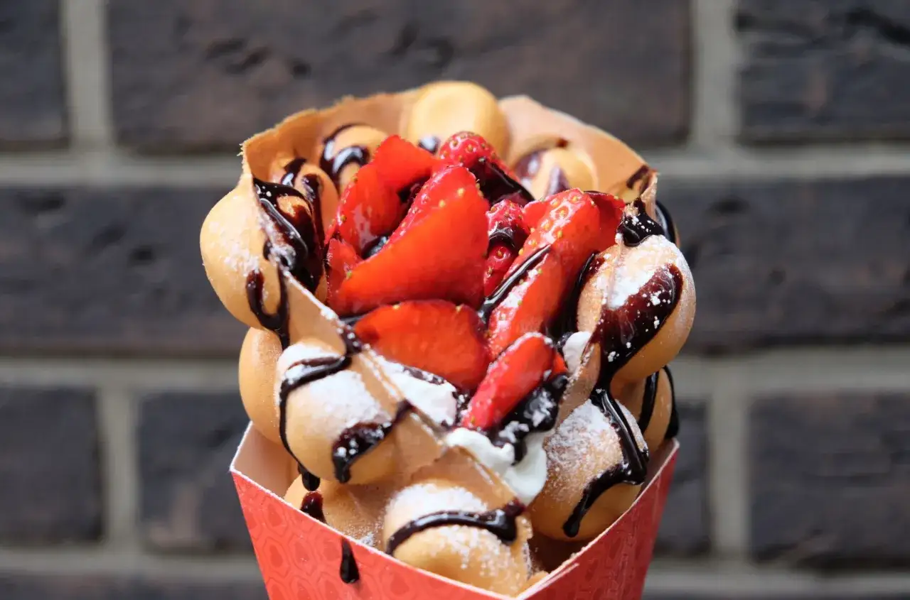 Ein k&ouml;stliches Bubble Eis mit frischen Erdbeeren, Schokoladensauce und Puderzucker, serviert in einem roten Papierbeh&auml;lter.