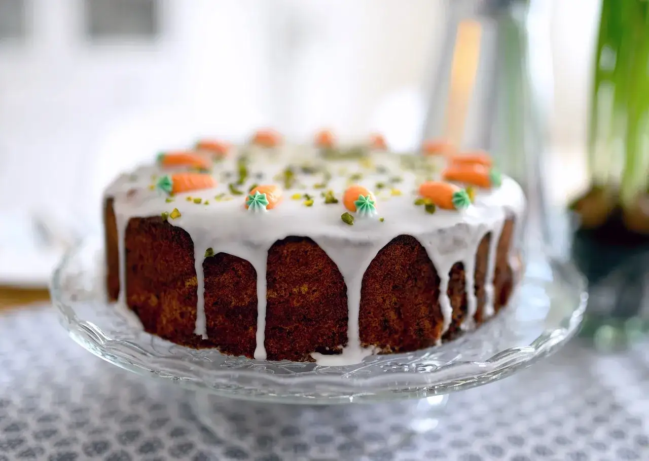 Ein köstlicher karottenkuchen glutenfrei, verziert mit Zuckermöhren und Pistazien, auf einer Glasplatte.