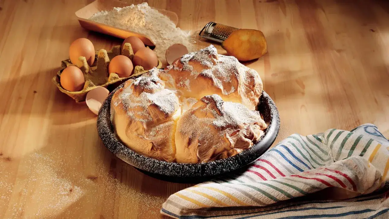 Ein frisch gebackener Salzburger Nockerl, best&auml;ubt mit Puderzucker, neben Eiern, Mehl und einer Zitrone.