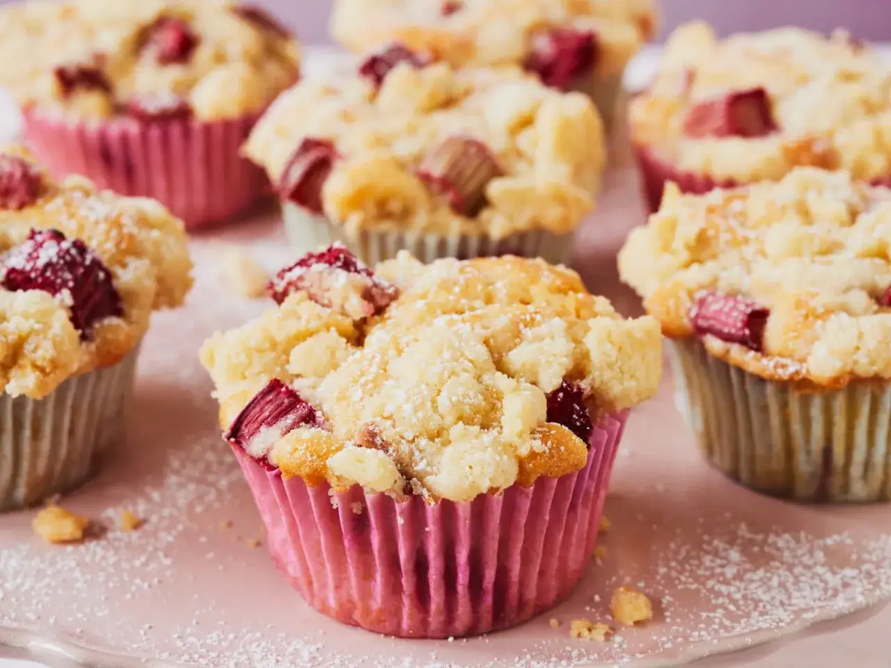 Saftige Rhabarber Muffins mit Streuseln, bestäubt mit Puderzucker, verlocken zum Genuss.
