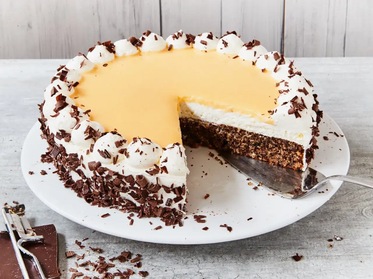 Eine einfache Torte mit gelbem Guss, weißer Sahne und Schokostreuseln. Ein Stück wurde bereits entnommen.