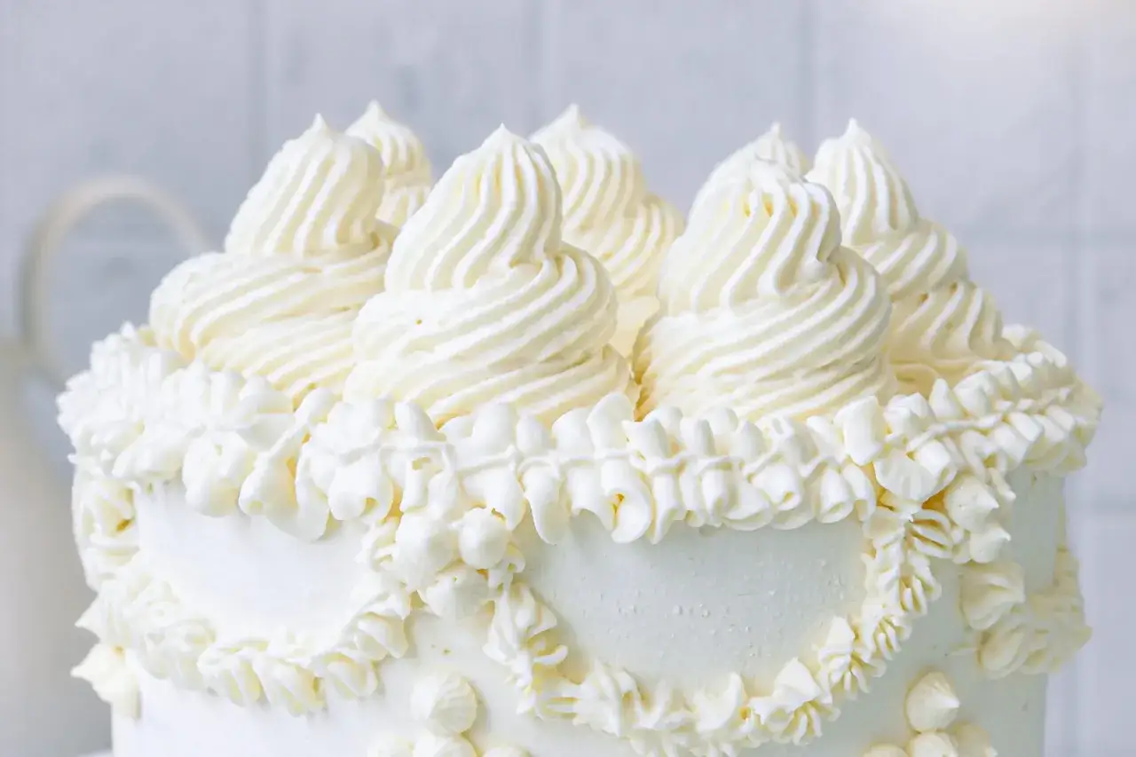 Ein weißer Kuchen, verziert mit üppigen Tupfen und Rüschen aus amerikanischer Buttercreme.