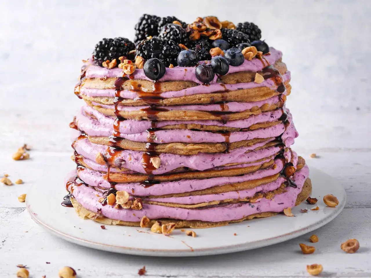 Eine beeindruckende Pfannkuchen Torte mit lila Creme, Beeren und Nüssen, beträufelt mit dunkler Sauce.
