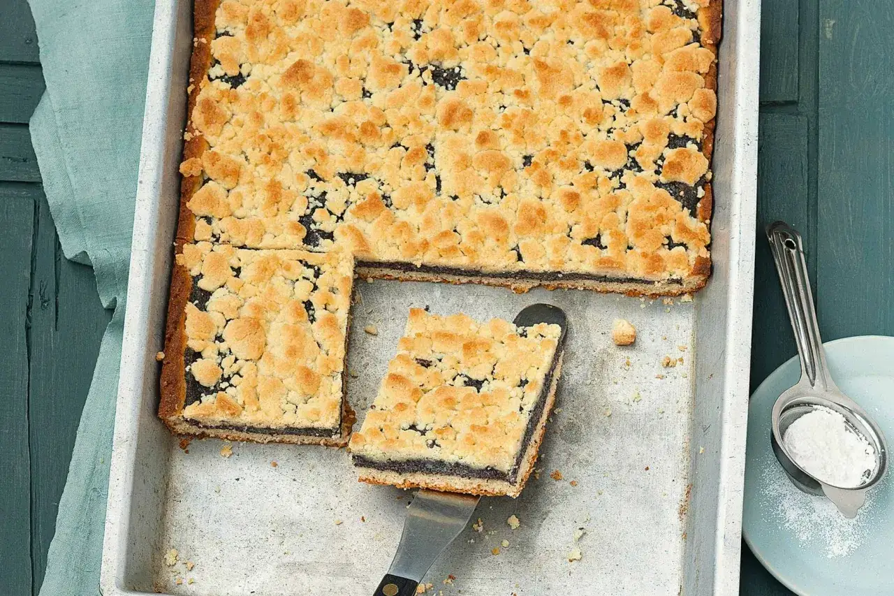 Ein frisch gebackener Frau Holle Kuchen mit Mohnfüllung und Streuseln wird aus einer Blechform gehoben.