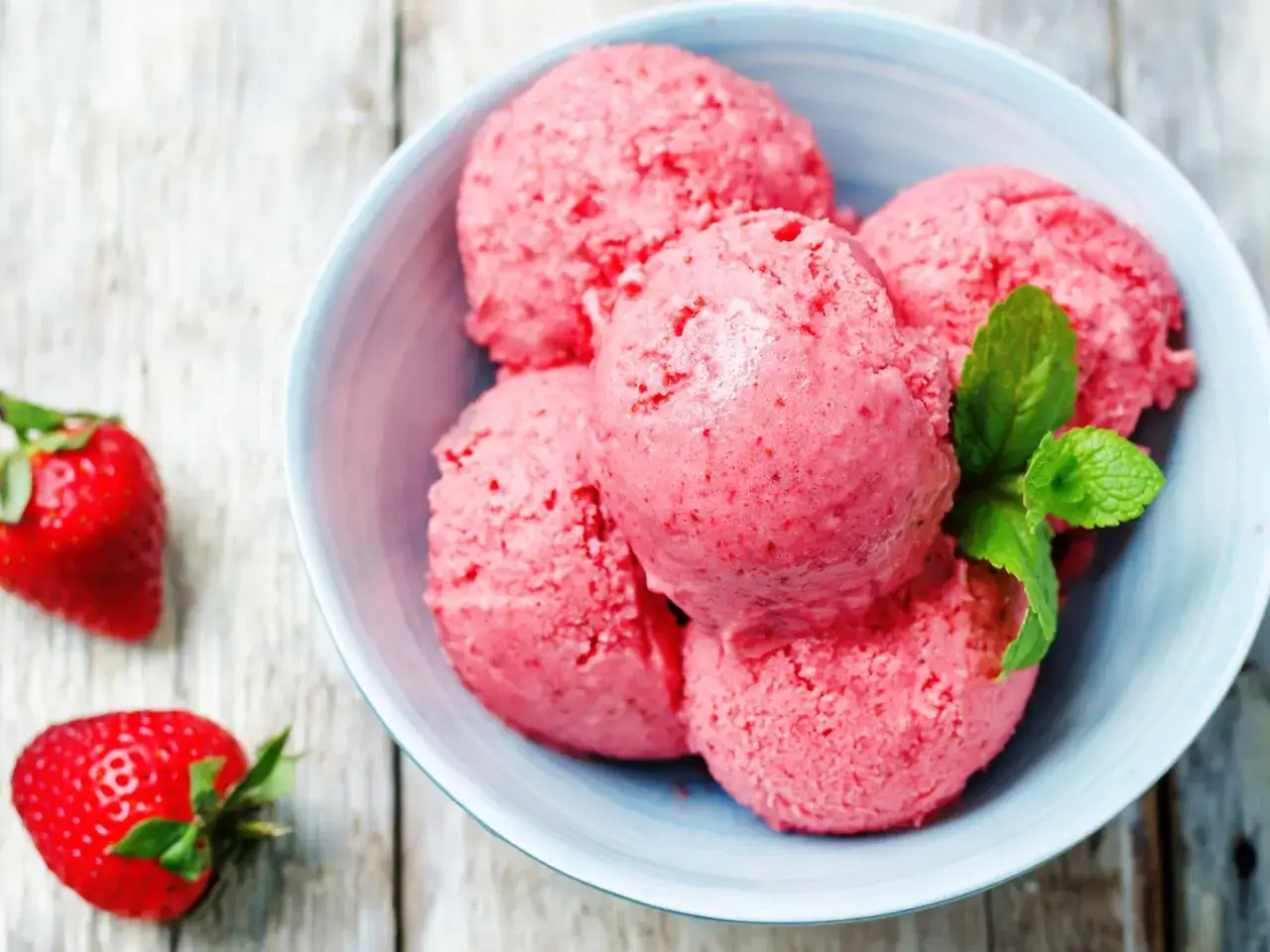 Schüssel mit leckerem Erdbeereis, das Lust macht, Erdbeereis selber machen. Frische Erdbeeren und Minze garnieren das cremige Dessert.