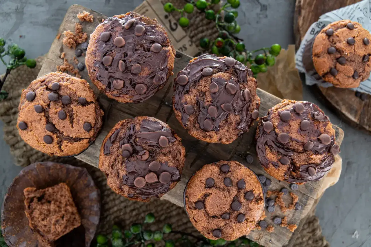 Saftige Nutella Muffins mit Schokostückchen, auf einem Holzbrett arrangiert. Ein Muffin ist angeschnitten und zeigt die feine Krume.