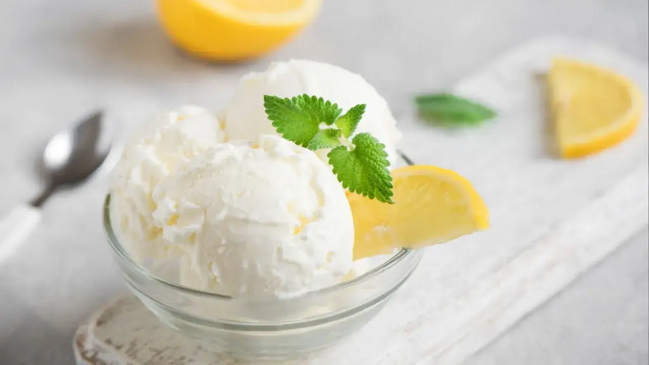 Schüssel mit cremigem Buttermilch Zitrone Eis, garniert mit Minze und Zitronenspalten. Ein Löffel liegt daneben.
