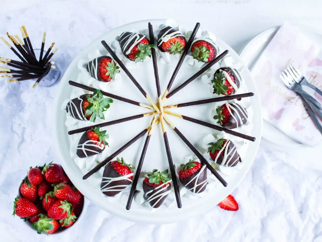 Erdbeer Mascarpone Torte mit Schokostreuseln und frischen Erdbeeren, dekoriert mit Schokostäbchen.