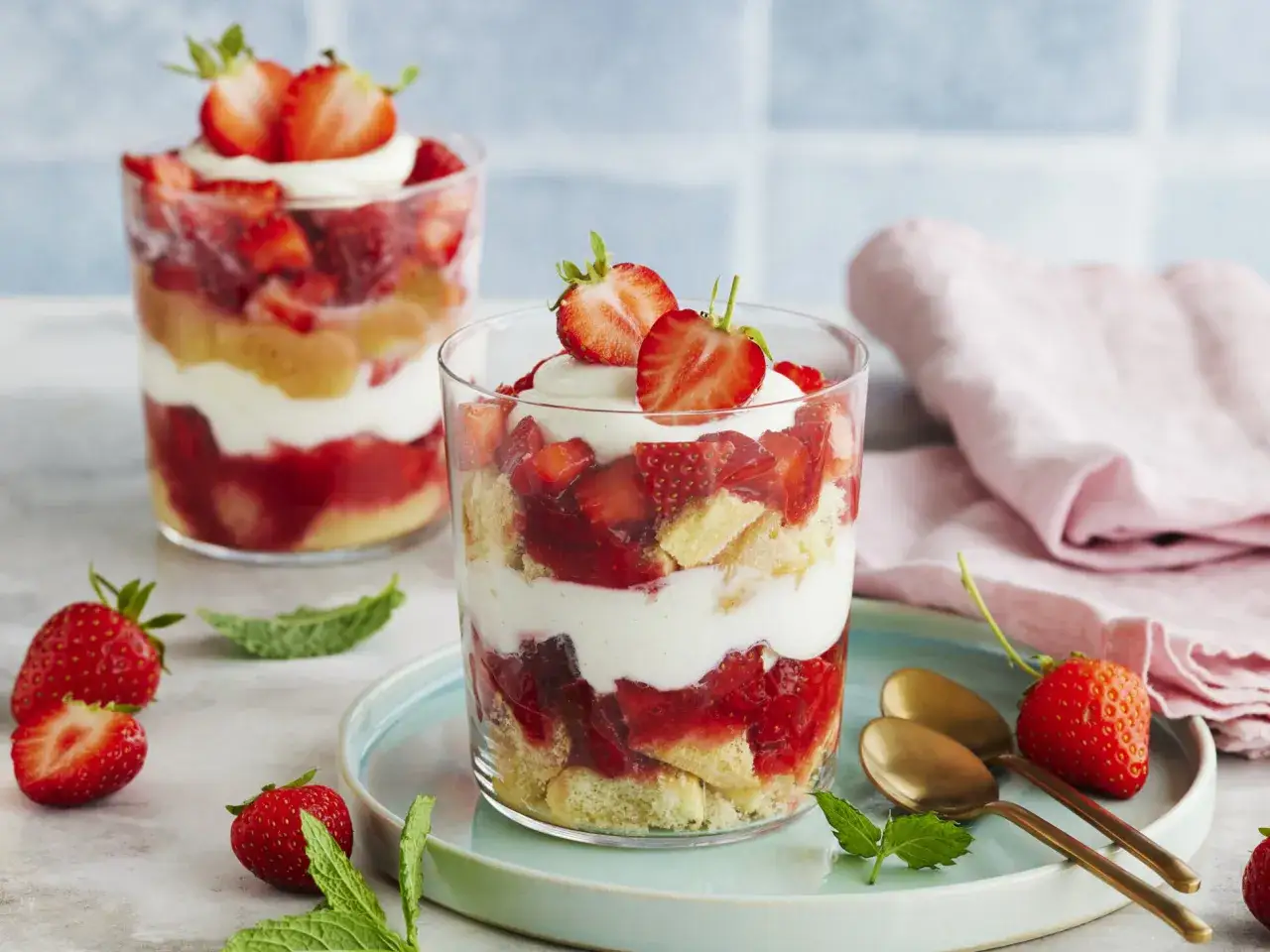 Zwei Gläser mit Erdbeer Tiramisu, geschichtet mit Biskuit, Erdbeeren und Creme, garniert mit frischen Erdbeeren.