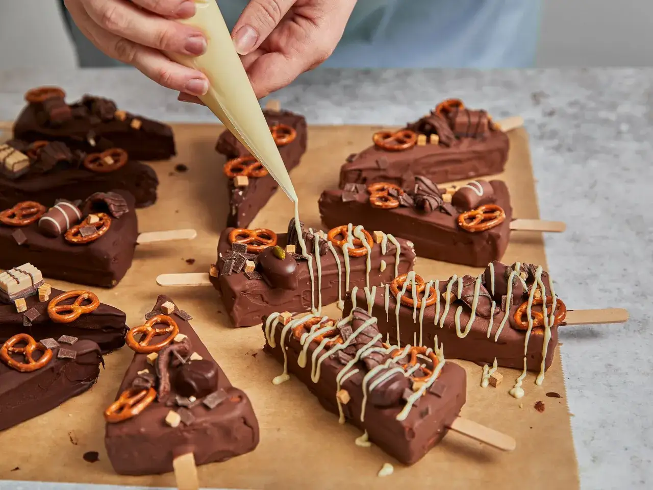 Schokoladige Cheesecake-Sticks mit Brezeln und Karamellst&uuml;cken werden mit wei&szlig;er Schokolade verziert.