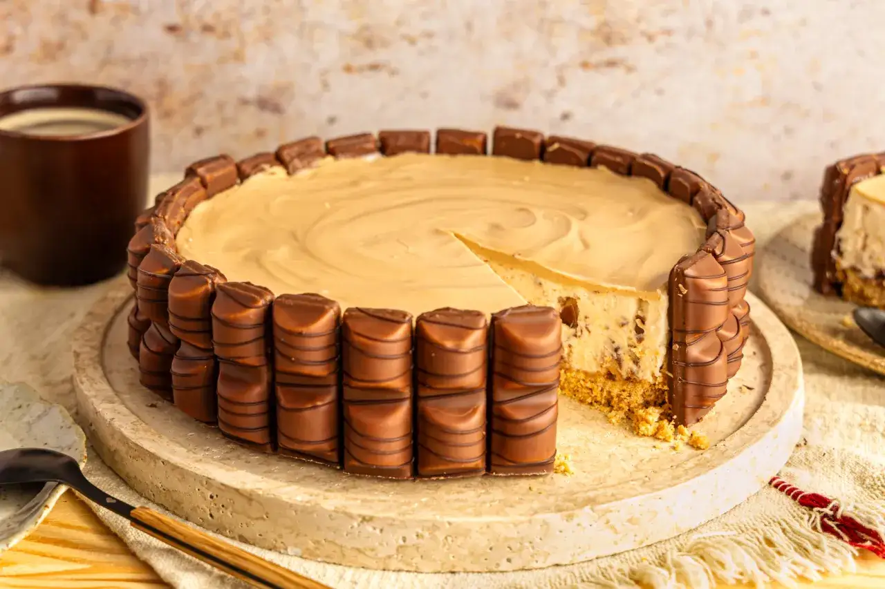Eine köstliche Kinder Bueno Torte, umhüllt von Schokoriegeln, mit einem Stück herausgeschnitten. Daneben eine Tasse Kaffee.