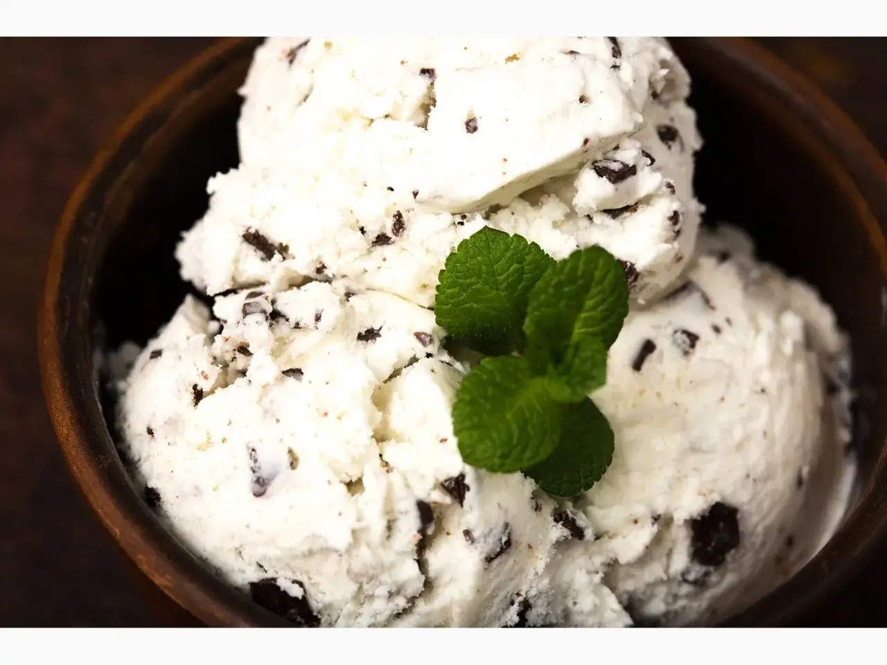 Cremiges Stracciatella Eis Rezept in einer Holzschale, garniert mit frischer Minze. Ein Genuss für heiße Tage!