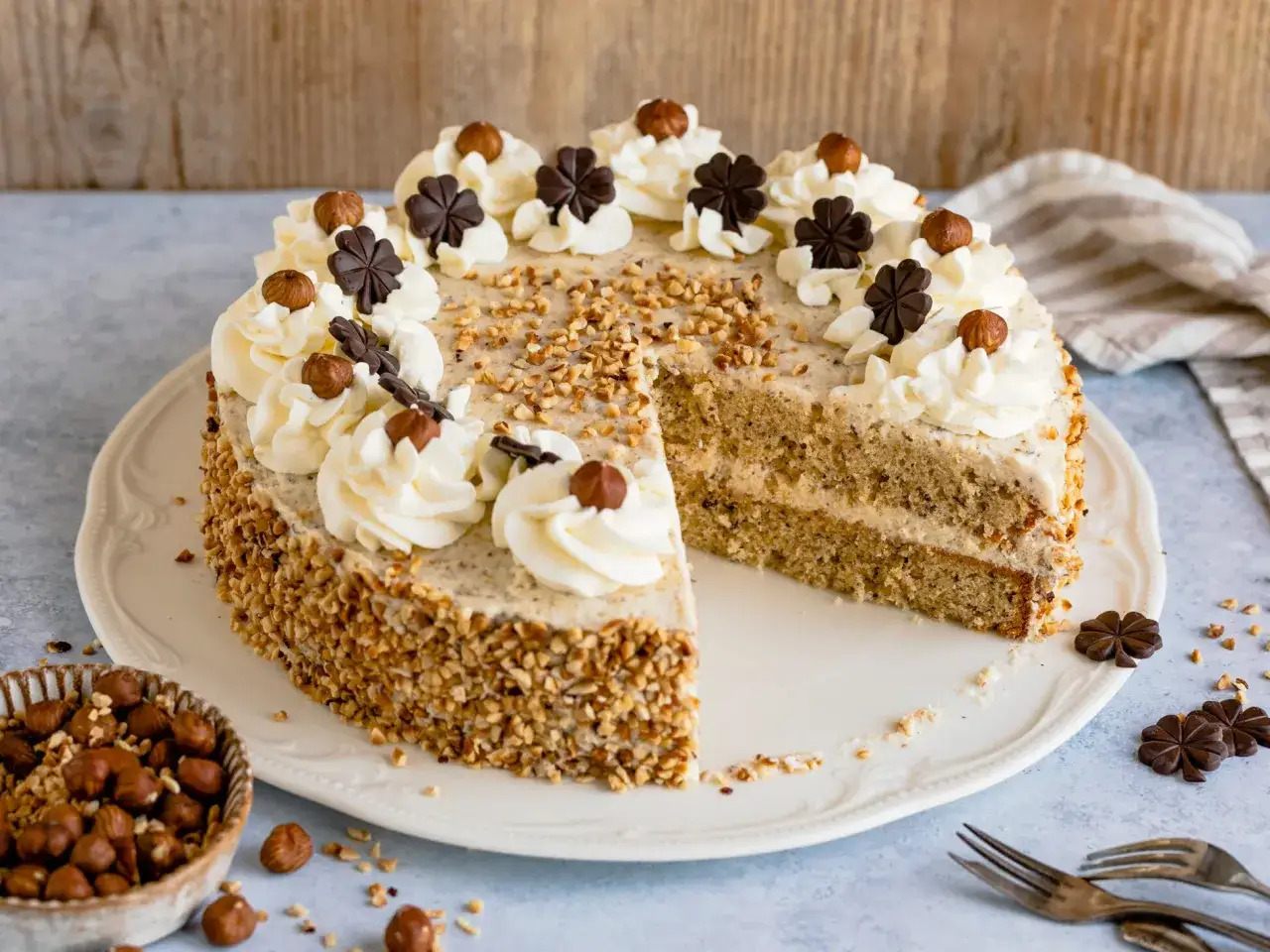 Eine köstliche Nusstorte, verziert mit Sahnetuffs, Haselnüssen und Schokoladenkleeblättern. Dieses nusstorte rezept ist ein Genuss!