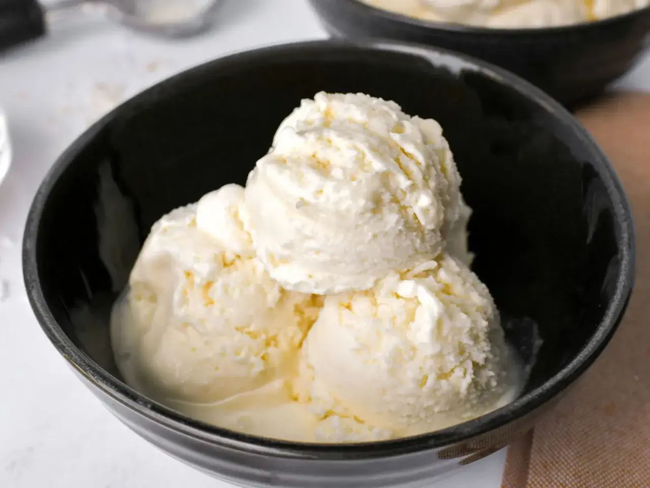 Cremiges Kokosnuss Eis selber machen: Drei Kugeln in einer schwarzen Schüssel, perfekt für heiße Tage.