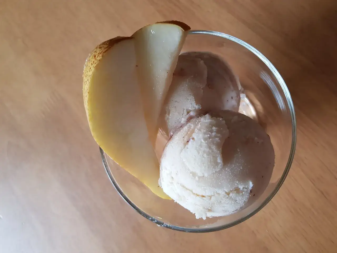 Ein Glas mit cremigem birnen eis, garniert mit einer frischen Birnenspalte.