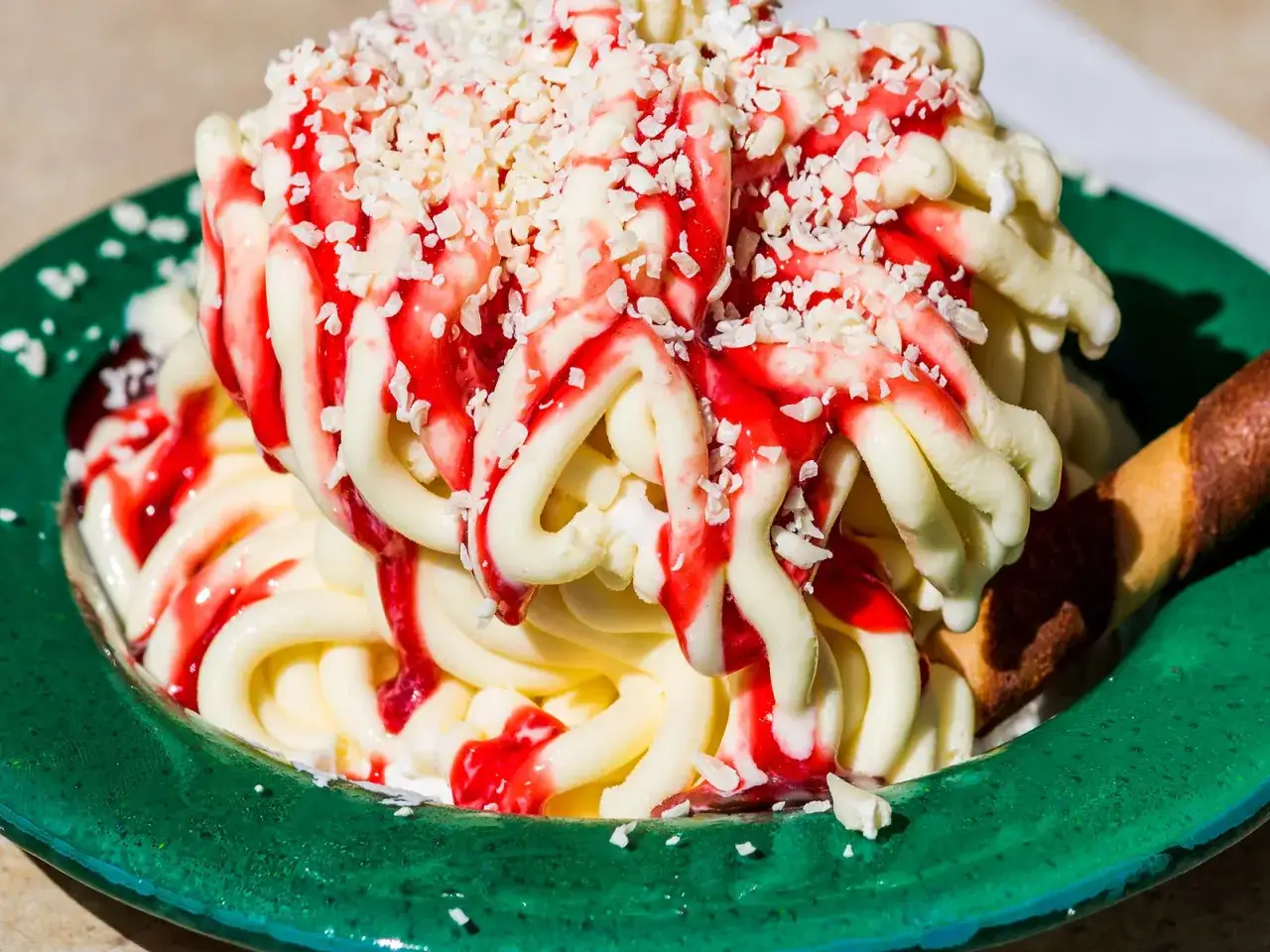 Spaghetti-Eis selber machen mit Kartoffelpresse: Cremiges Vanilleeis mit Erdbeersoße und weißen Schokostreuseln in einer grünen Schale.