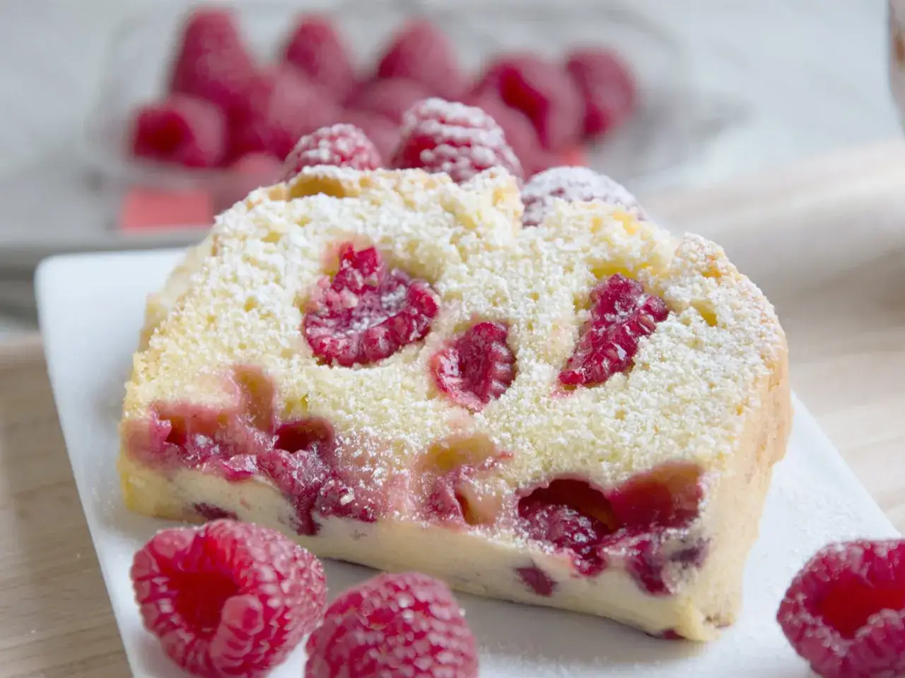 Ein Stück saftiger Vanille Kuchen mit frischen Himbeeren, bestäubt mit Puderzucker.